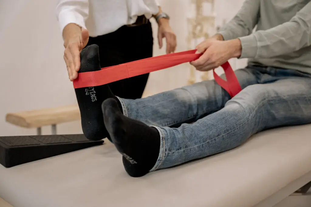 Die Schmerztherapeutin Gabriele Cunskis zeigt einem Patienten, wie man eine Engpassdehnung am Knie mit der Übungsschlaufe durchführt.